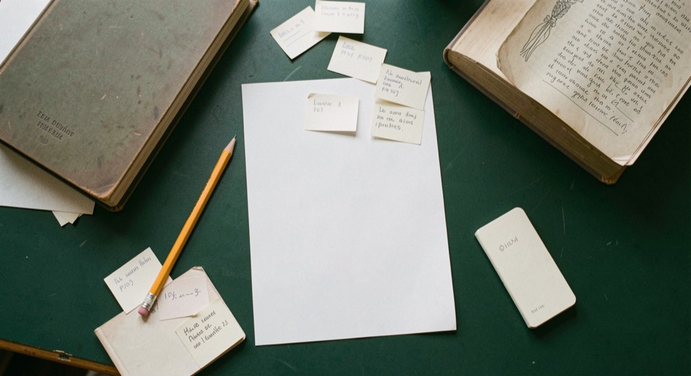Overhead documentary photograph of index cards, a pencil, a book and a small notebook on a deep green desk, blank paper with no legible writing, soft window light. Distinct supporting card P101 1 composition for this editorial entry.