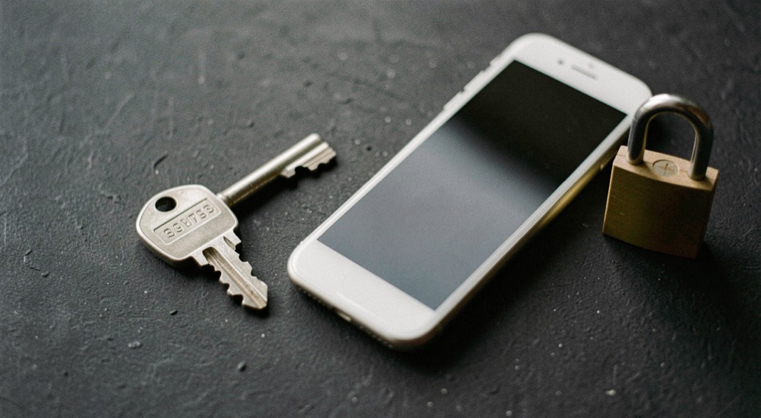 Documentary photograph of a metal key, a phone with a blank dark screen and a small padlock on a charcoal surface, no visible writing, controlled side light. Distinct supporting card P304 3 composition for this editorial entry.
