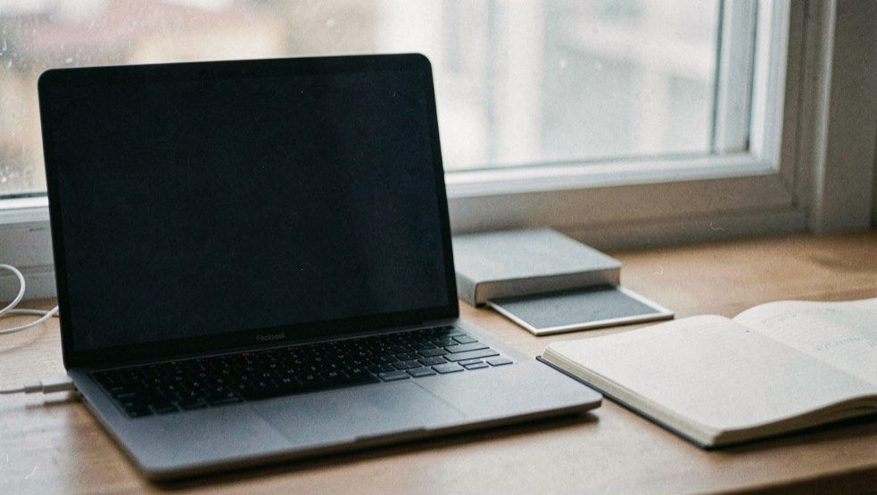 Documentary photograph of a laptop with a completely blank dark screen beside a notebook, a small privacy shutter and a window reflection, no readable interface, cool morning light. Distinct supporting card P201 2 composition for this editorial entry.