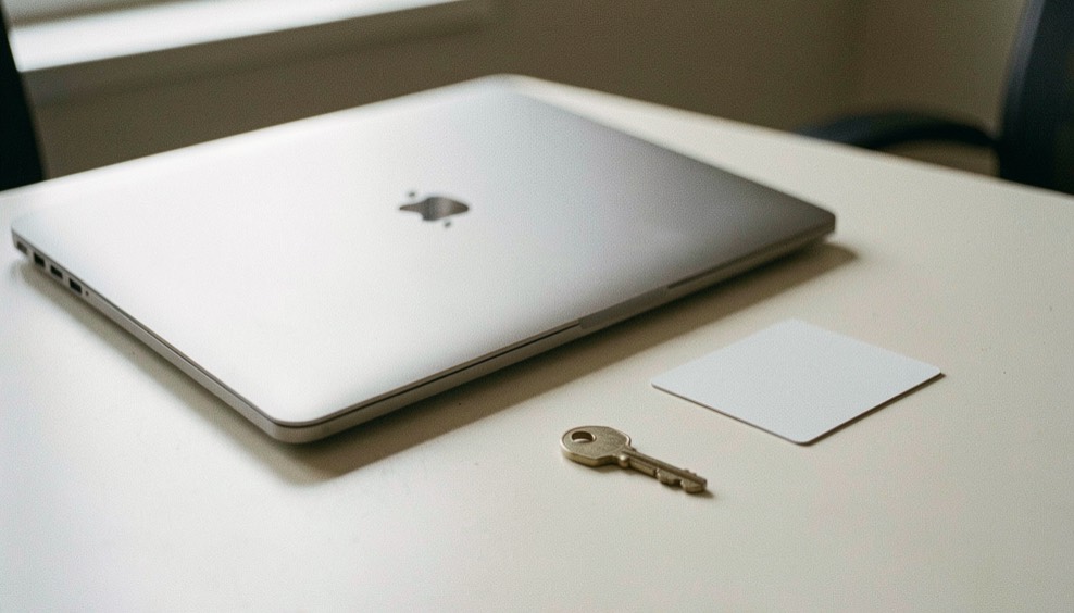 Documentary photograph of a closed laptop, a blank privacy card and a small key on a pale desk, no readable text, quiet diffuse light. Distinct lead composition for this editorial entry.